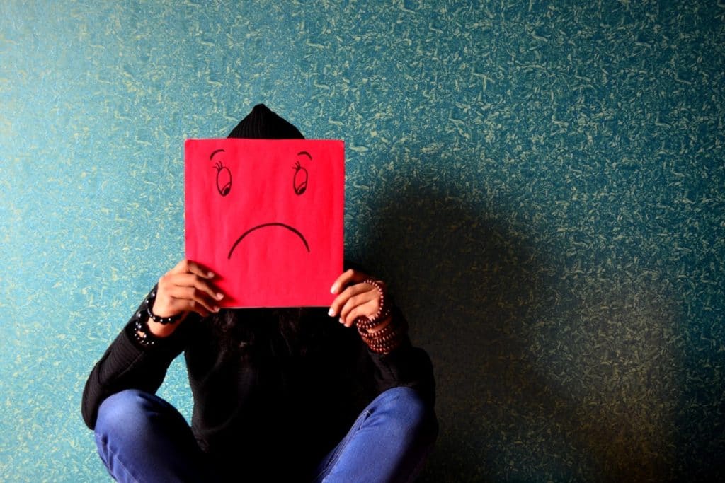 Personne tenant un papier avec un visage triste dessiné dessus pour montrer qu'il est important de prendre une assurance santé quand on rentre en France après une longue expatriation.