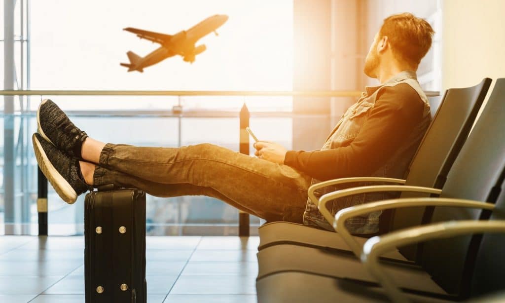 Homme assis et attendant son avion à l'aéroport, content d'avoir pris une assurance annulation car son vol a été annulé 